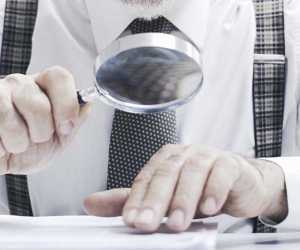 Senior corporate businessman reading paperwork using a magnifier, he is checking carefully an agreement